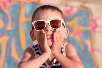 smiling little boy wearing sunglasses closed his mouth with hands