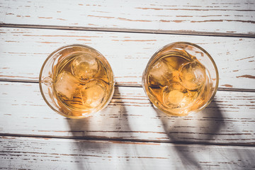 Whiskey glasses with ice cubes on white wooden table