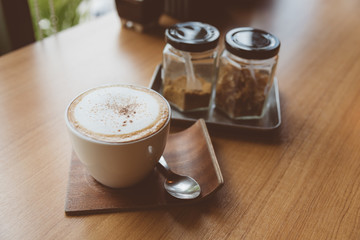 Hot coffee in white cup with brown sugar in glass jar Placed on the bar by the window in selective focus.