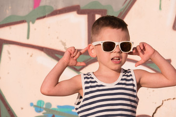 dreaming little kid wearing sunglasses and striped vest on graffiti background