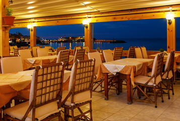 traditional European cafe in night on island of Crete Greece night. Wooden chairs with white tablecloths on the Bay. Chersonissos Greece