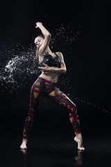 The girl dances on the floor covered with water on a black background and water splashes around her