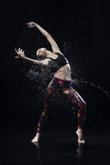 Fototapeta na wymiar The girl dances on the floor covered with water on a black background and water splashes around her
