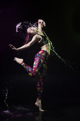 The girl dances on the floor covered with water on a black background and water splashes around her