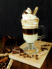 Coffee cocktail with whipped cream in an Irish coffee mug surrounded by coffee beans, cinnamon and chocolate bars