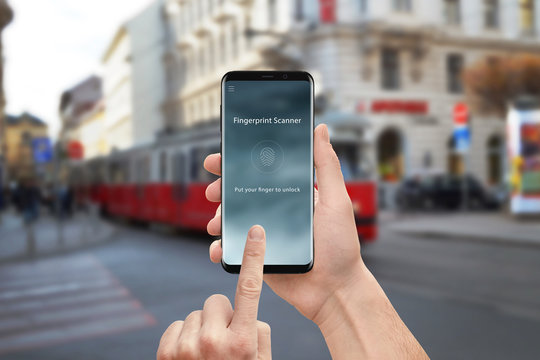 Fingerprint scanner security app on moder mobile phone. Man holding and touch round phone screen. Street in background.