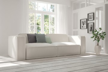 Fototapeta premium White room with sofa and green landscape in window. Scandinavian interior design. 3D illustration