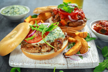 Delicious Bagel Pork sandwiches with vegetable and Tzatziki Sauce and Fries on white board.