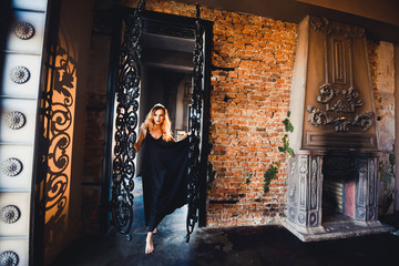 close-up portrait of young beautiful red-haired girl in the image of a Gothic witch on Halloween on a background of wax candles, fire, magic crystals and stones in the black dress conjures