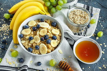 Bowl of Healthy Breakfast oatmeal with ripe blueberries, banana, honey, almonds and green grape. Top view
