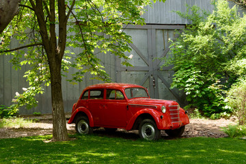 Red retro car in a garden amongst trees