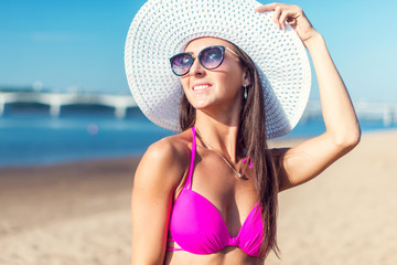 Portrait of beautiful young woman in hat posing in bikini on the beach