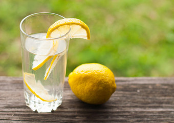 Cool lemonade in a glass sink in the garden. On a wooden table on a background of green grass.