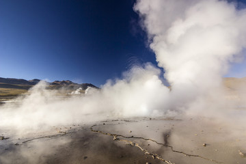 steam of geyser tatio against sun at sunrise with people standing