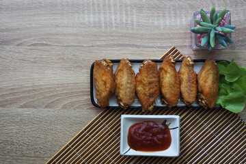 Fried chicken wings in a square dish, placed on a brown wooden floor and have ketchup next to it. copy space