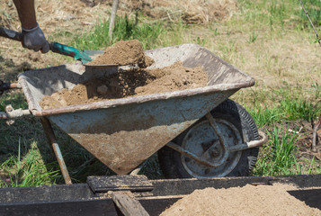 Fototapeta na wymiar The man pours the clay out of the wheelbarrow with a shovel