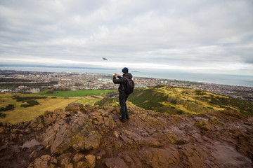 Tourist taking pictures of Edinburgh city from Arthur's Seat hill