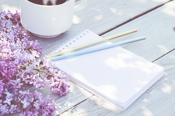 Cup of coffee, notepad, and a lilac branch on the white wooden table