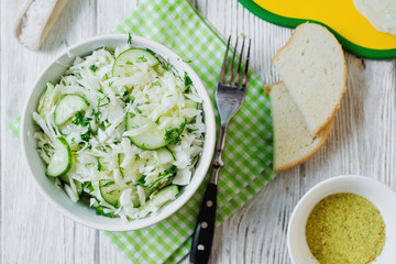  vegetarian Healthy food, light, low calorie fitness salad of fresh cucumbers, cabbage and dill with olive or sunflower oil, spices and salt on a light wooden background 