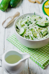  vegetarian Healthy food, light, low calorie fitness salad of fresh cucumbers, cabbage and dill with olive or sunflower oil, spices and salt on a light wooden background 
