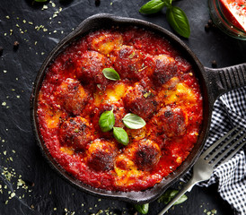 Meatballs in tomato sauce with addition cheese and fresh basil on iron pan, black background