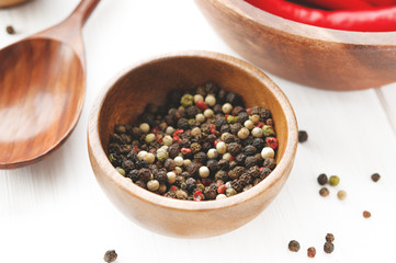 Bowl of black, white and red pepper on white wooden table