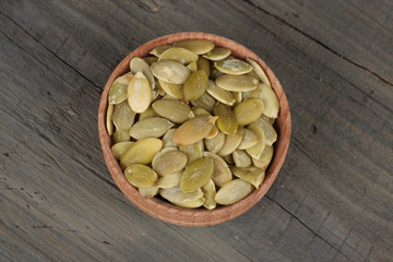 Pumpkin seeds in wooden bowl on wooden background top view with copy space