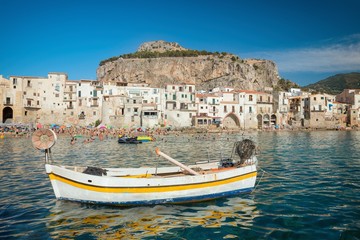 Fototapeta na wymiar Unidentified people on sandy beach in Cefalu, Sicily, Italy