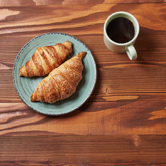 food plate of donut and croissant with mug of coffe on wooden background
