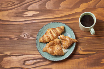 food plate of donut and croissant with mug of coffe on wooden background