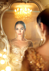 Beauty glamour lady looking in the mirror. Gorgeous woman in beautiful evening dress in luxurious...