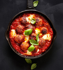 Meatballs in tomato sauce with addition cheese and fresh basil on iron pan, black background