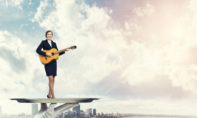 Fototapeta na wymiar Attractive businesswoman on metal tray playing acoustic guitar against cityscape background