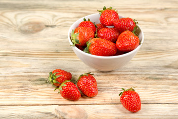 Ripe strawberry in a white bowl on a wooden background