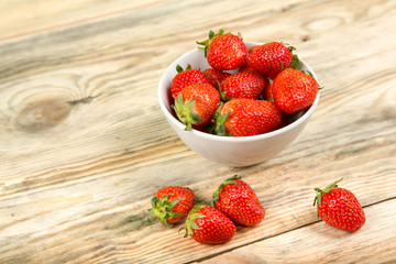 Ripe strawberry in a white bowl on a wooden background