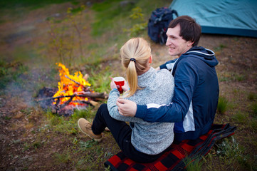 Young couple traveler sitting by the fire and drinking tea