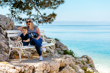 Mother and son sitting on the bench at the rocky beach