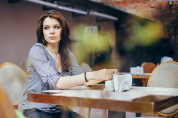 A young pensive woman dreams about something in anticipation of a waiter in a modern cafe interior. Shooting through the foreground.