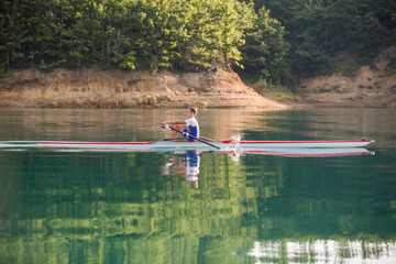 A Young single scull rowing competitor paddles on the tranquil lake