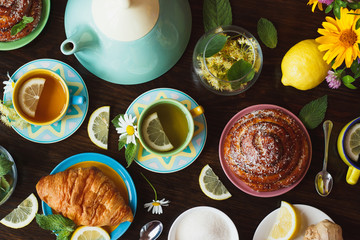 Cups of herbal tea with lemon and mint leaves, ginger root and croissant on the wooden background