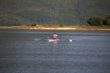 A Young single scull rowing competitor paddles on the tranquil lake