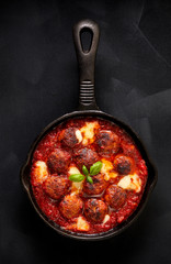 Meatballs in tomato sauce with addition cheese and fresh basil on iron pan, black background, top view