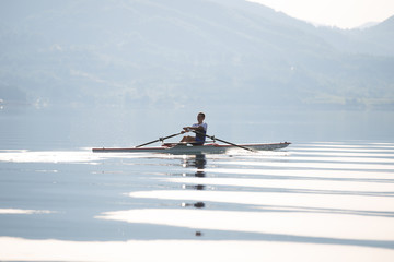 A Young single scull rowing competitor paddles on the tranquil lake