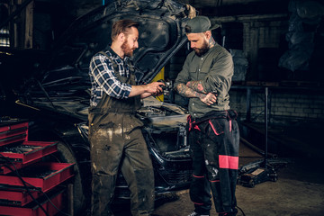 Fototapeta na wymiar Two bearded mechanics inspecting car's engine parts.