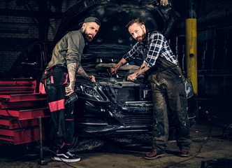Fototapeta na wymiar Two mechanics fixing car's engine in a garage.