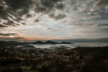 Fototapeta na wymiar Village in the mountains with clouds and fog and sun in sunset