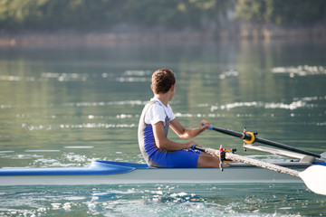 A Young single scull rowing competitor paddles on the tranquil lake