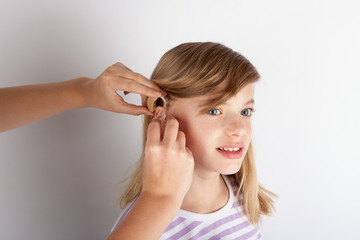 Close up of a Doctor's hands fitting a hearing aid for a young girl patient .