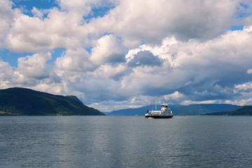 The ferry sails along the Norwegian fjord in Sunny day with beautiful clouds and mountains in background. The horizontal frame.