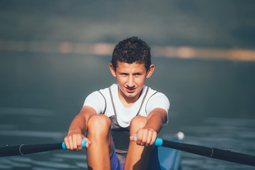 A Young single scull rowing competitor paddles on the tranquil lake